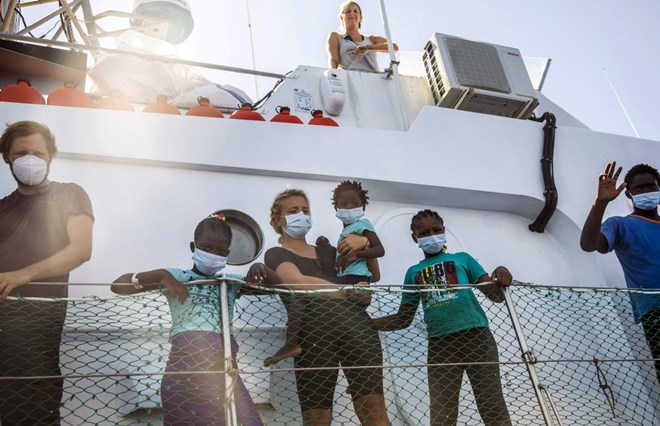 Crew members and rescued workers stand on the deck of the Louise Michel rescue vessel, a French patrol boat currently manned by activists and funded by the renowned artist Banksy in the Central Mediterranean sea, at 50 miles south from Lampedusa, , Friday, Aug. 28, 2020. A Berlin-based group says it has begun migrant rescue operations in the Mediterranean Sea with a bright pink former navy vessel sponsored by British artist Banksy. The group operating the MV Louise Michel, a sleek 30-meter (98-foot) ship named after a 19th century French feminist and anarchist, said late Thursday that it rescued 89 from an inflatable boat in distress. (AP Photo/Santi Palacios)