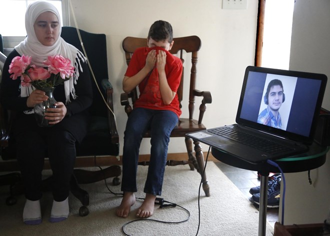 Ten-year-old Syrian Amjud Moustafa Rifat uses his shirt to wipe away tears on Tuesday, Feb. 20, 2018, in Columbus, Ohio, as he and his 18-year-old sister, Fatima, listen to a song their brother, Hasib, wrote for the family. Hasib, 16, is still in the Middle East and has been separated from his family for more than 18 months as he awaits a U.S. visa. Their father, Rifat Moustafa, an international lawyer who says he was tortured for protesting human rights violations, was granted asylum and his wife and four other children followed in 2016, before President Trump was elected. They were hoping Hasib could come shortly after, but resettlement officials say the Trump administration’s travel ban on refugees from mostly Muslim countries has very likely caused further delays. (AP Photo/martha Irvine)