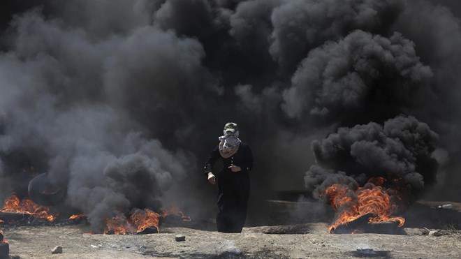 A Palestinian woman walks through black smoke from burning tires during a protest on the Gaza Strip's border with Israel on May 14, 2018.