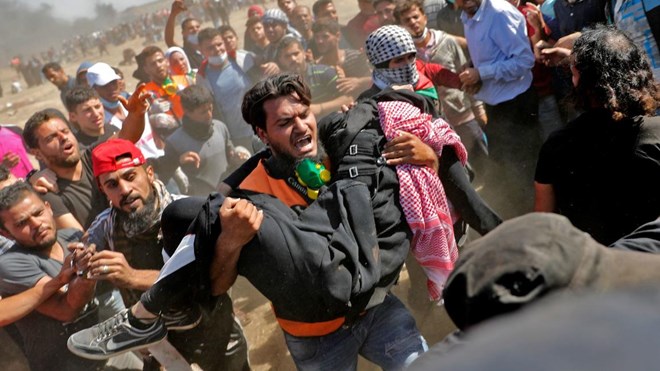Palestinians carry a demonstrator injured during clashes with Israeli forces near the border between the Gaza strip and Israel east of Gaza City on May 14, 2018, as Palestinians protest over the inauguration of the US embassy following its controversial move to Jerusalem.