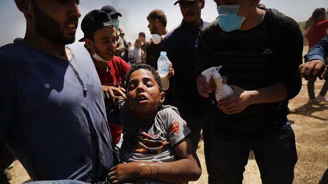A child overcome by tear gas is rushed to medics at the border fence with Israel as mass demonstrations continue on May 14, 2018 in Gaza City, Gaza.